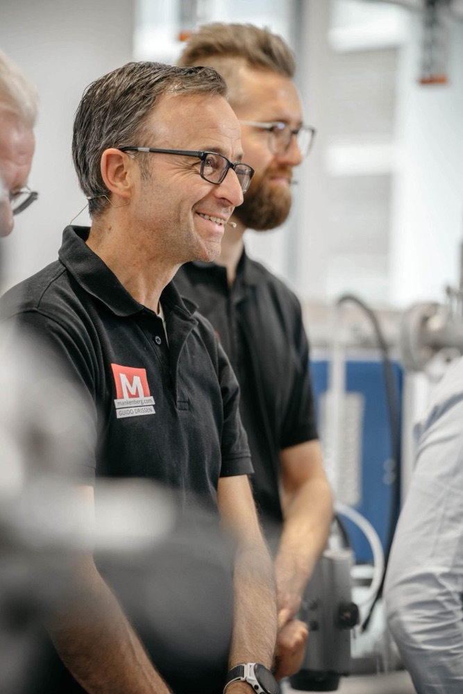 Zwei lachende Kollegen in Poloshirts bei einer Werksführung